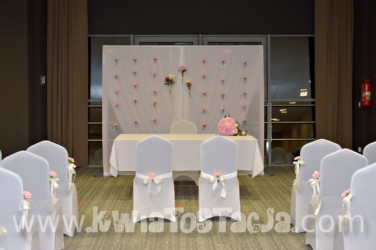 Florystyczna dekoracja stołu i ścianki za nim. Dekoracja sali na uroczystość zawarcia związku małżeńskiego